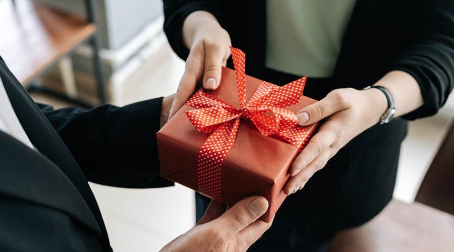 Close-up view of hands of unrecognizable woman giving red gift box tied to bow handed to man.
