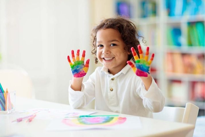 Child drawing rainbow. Paint on hands.